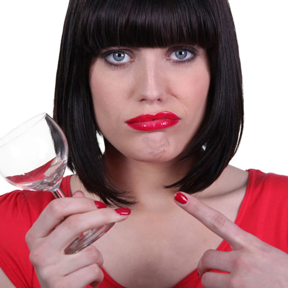 Frau mit roten Lippen zeigt frustriert auf ein Glas.