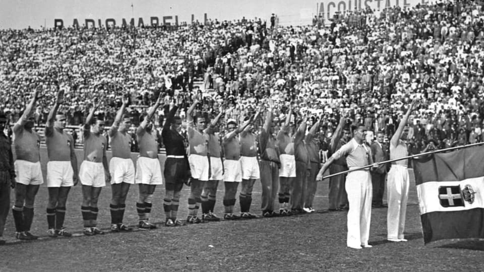 Schwarzweiss-Bild: Die italienische Fussballnationalmannschaft streckt die rechte Hand zum Himmel.