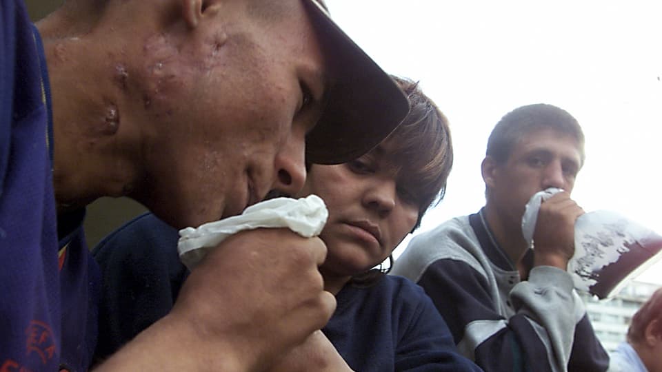 Drei mit Narben übersähte Jugendliche halten Plastiksäcke an den Mund.