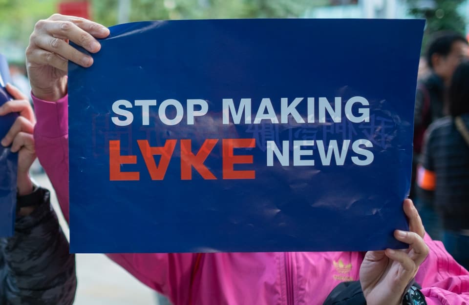Zwei Hände halten ein "Stop Making Fake News"-Schild in die Luft.