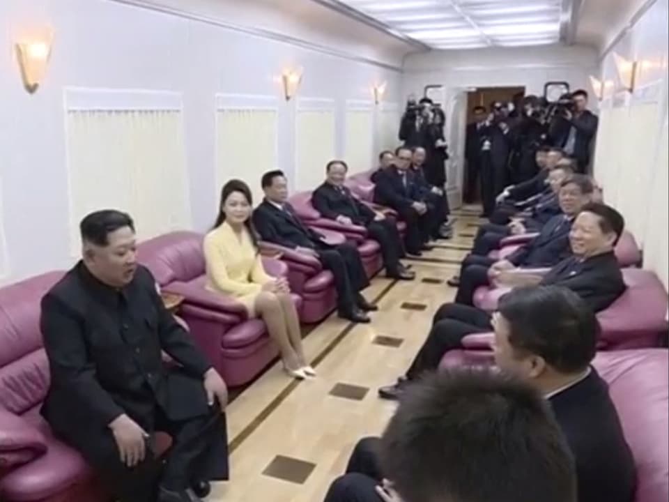 Kim is on the train with people in pink chairs