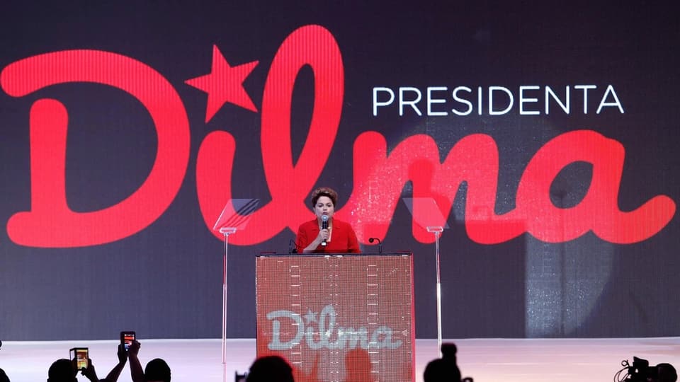 Rousseff an einem Rednerpult. An der Wand prangt ihr Vorname.