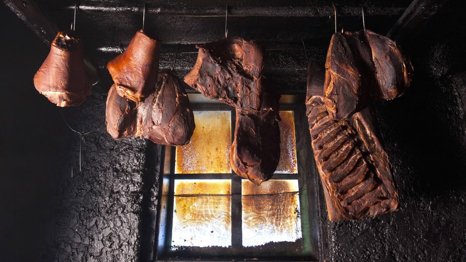 Blick in eine Räucherkammer, in der Schinken und andere grosse Stücke Fleisch hängen.