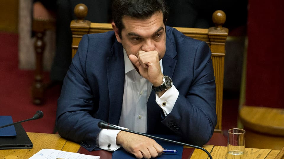 Tsipras sitzt im Parlament, eine Hand vor dem Mund, die Backen aufgeblasen.
