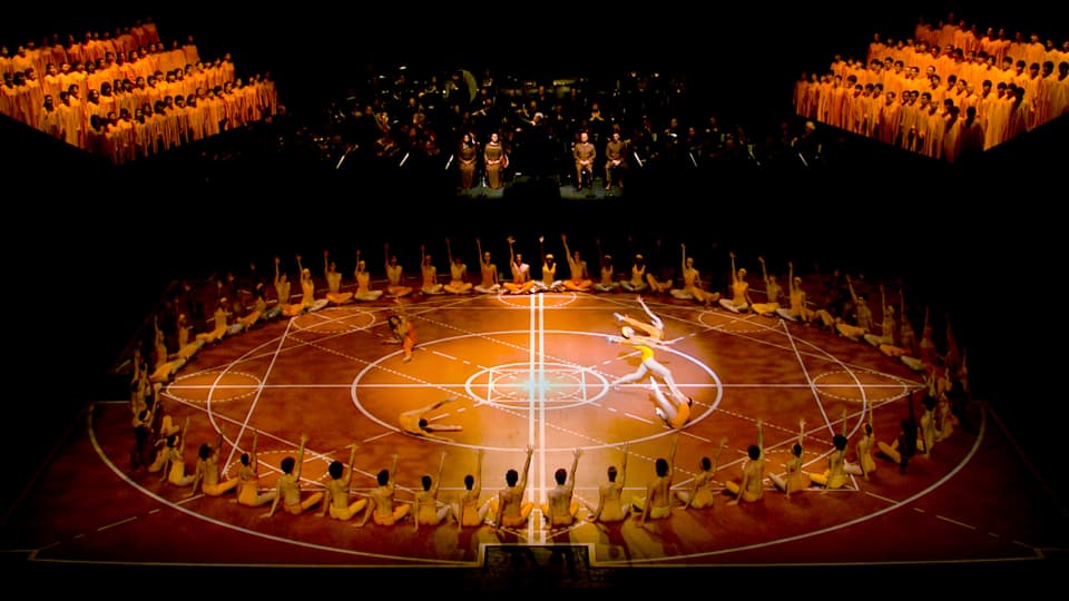 Eine Bühne: Über 40 Tänzerinnen bilden einen Kreis. Darum zwei Blöcke mit Sängern und ein Orchester.