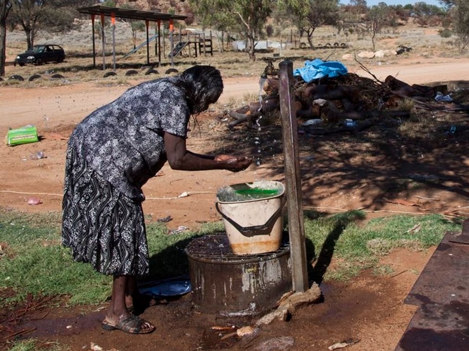Eine Frau trinkt an einem Brunnen Wasser
