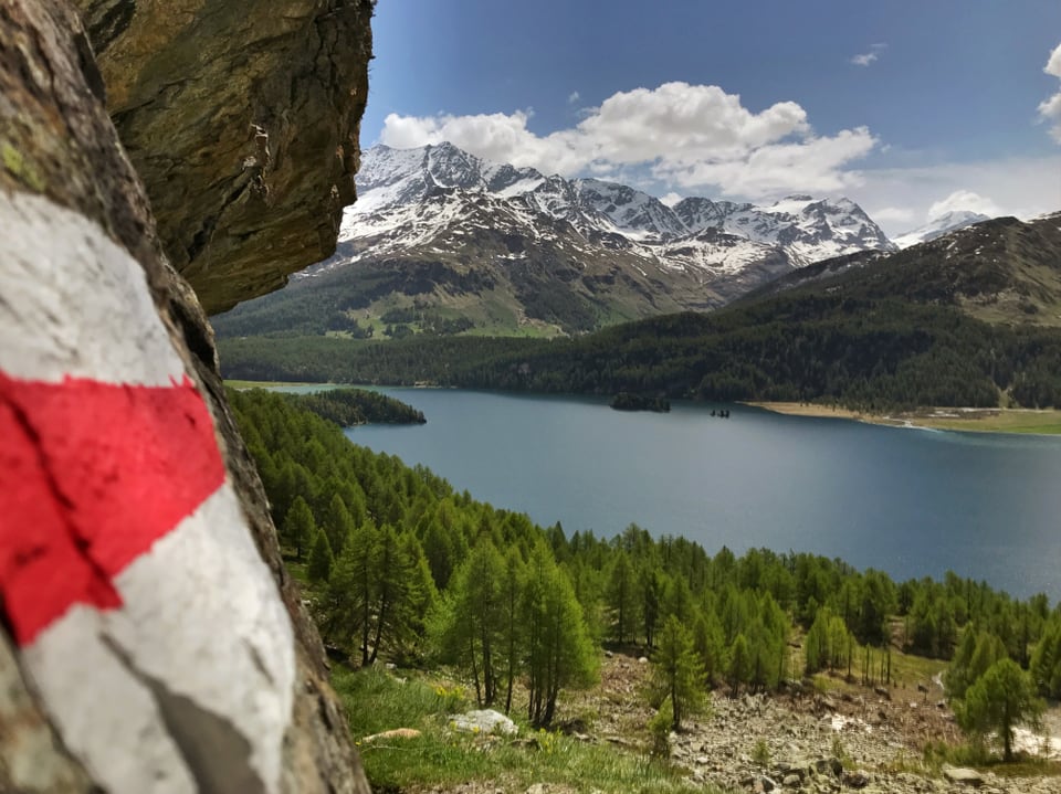 rot-weisse Wandermarkierung auf einem Stein, im Hintergrund ein blauer See