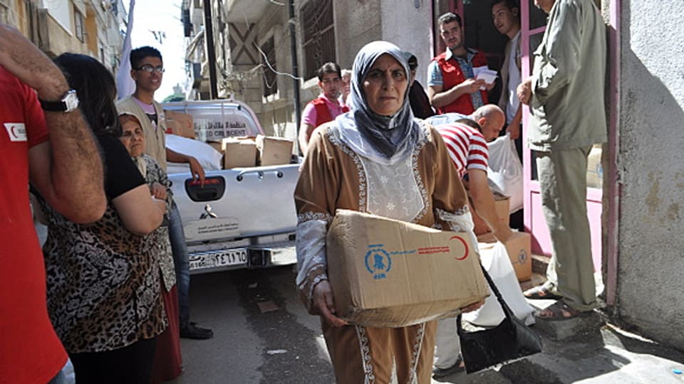 Ein Frau in Syrien trägt eine kleine Kartonschachtel mit Lebensmitteln.