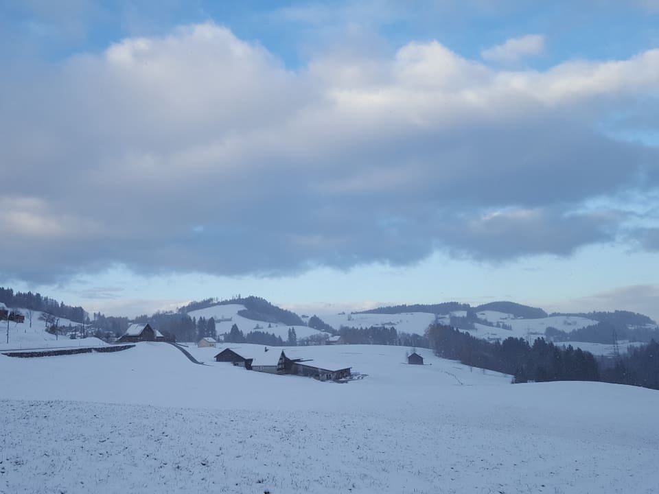 Das hügelige Appenzellerland liegt unter einer dünnen Schneedecke. Am Himmel sind blaue Wolkenlücken.