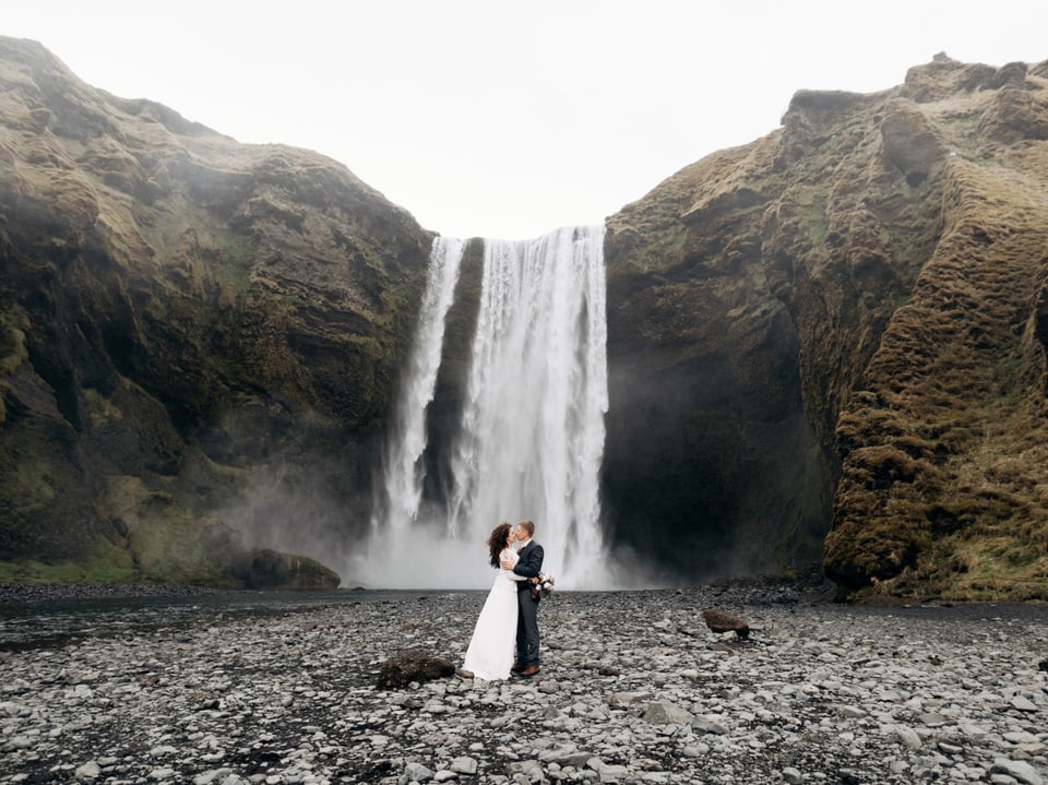 Ein Brautpaar küsst sich vor einem Wasserfall in Island.