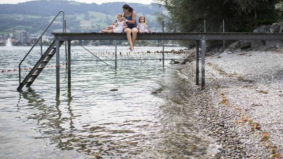 Eine Frau sitzt mit ihren Kindern auf einem Steg am Bodensee.