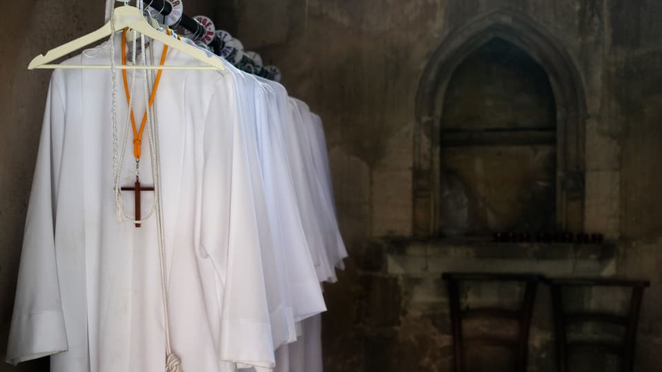 Weisse Priestergewänder hängen an Kleiderbügeln an einer Stange in einer alten Kirche.