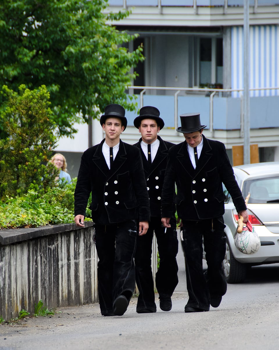 Drei Männer in schwarzen Anzügen und mit Hut.