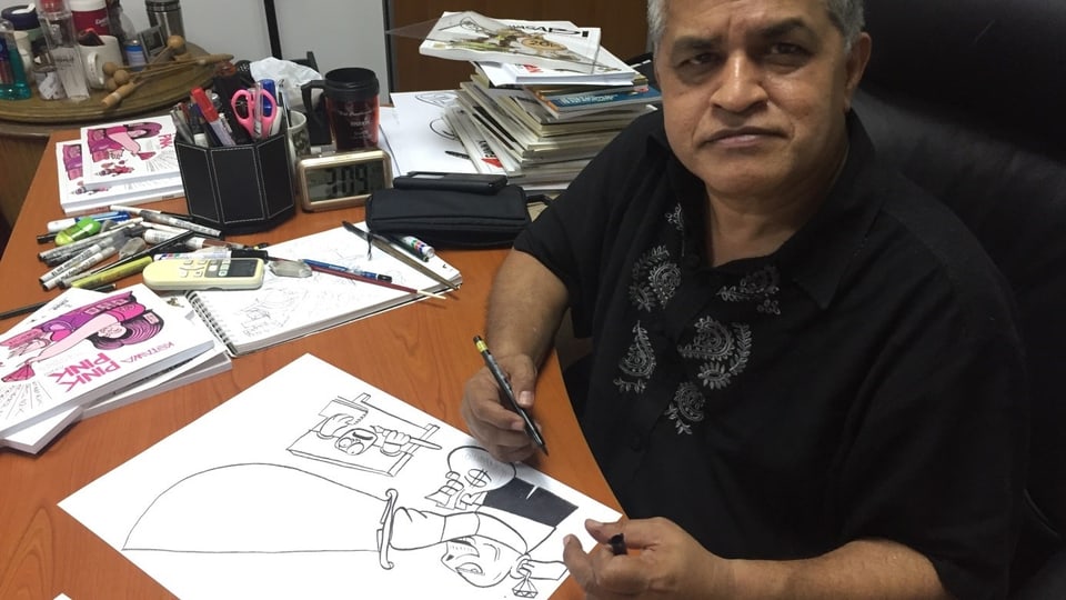 Karikaturist Zunar, vor einer Zeichnung sitzend