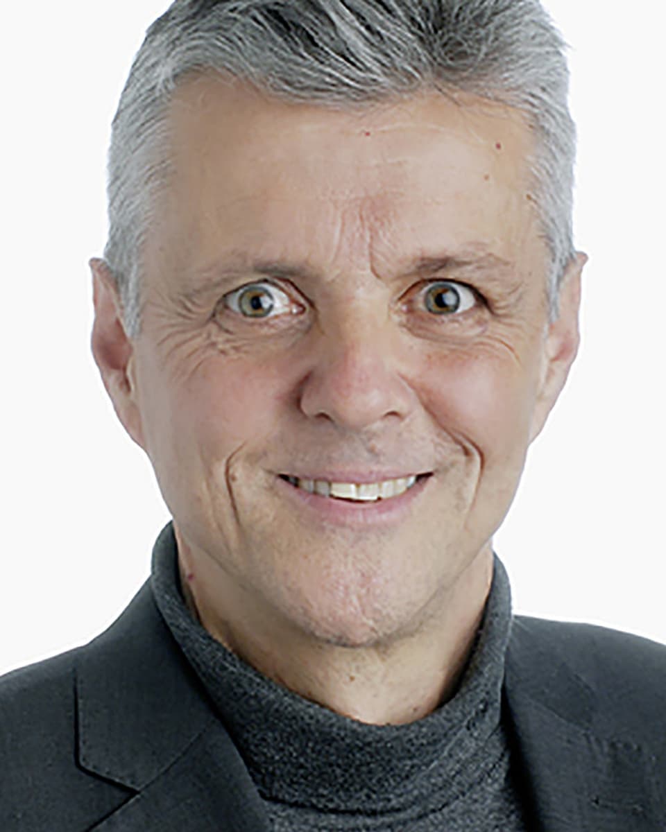 Ein Foto von einem lächelnden Mann mit grauen Haaren und grauem Jackett.