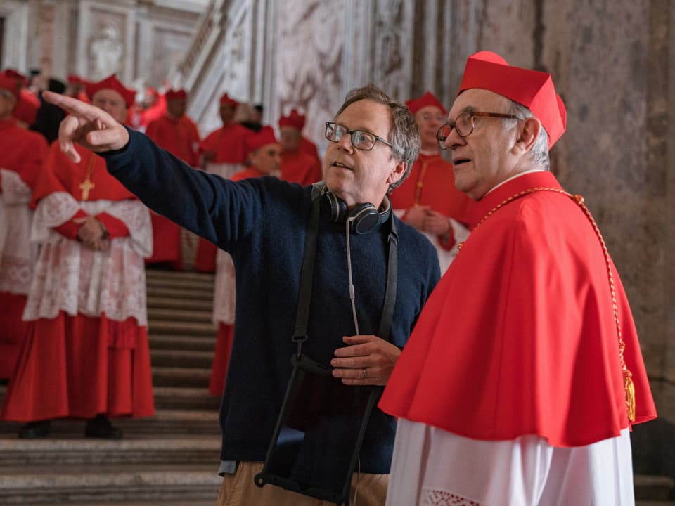 Mann (Regisseur) zeigt mit dem Finger nach links, neben ihm steht ein Kardinal und schaut in dieselbe Richtung