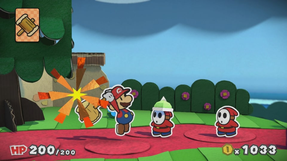 Ein Shy Guy mit grünem Helm mit Spitze. Mario zeigt ihm, wo der Hammer hängt. Auf dem Kopf.
