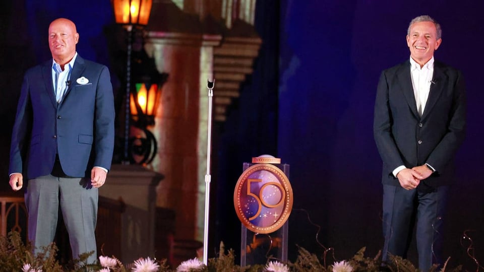 Two men standing on stage. A floral ornament and label can be seen