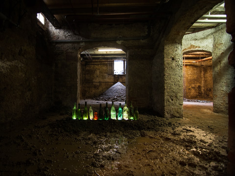 Duinkler Keller, darin stehen Flaschen aufgereiht und diese sind beleuchtet.