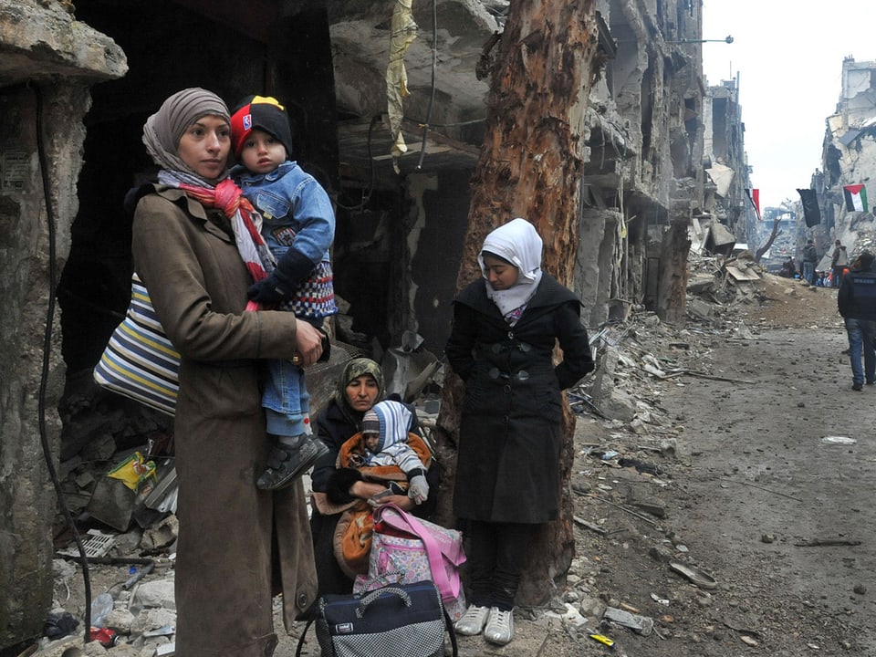 Frauen stehen mit Kindern auf dem Arm an einer Strassenecke.