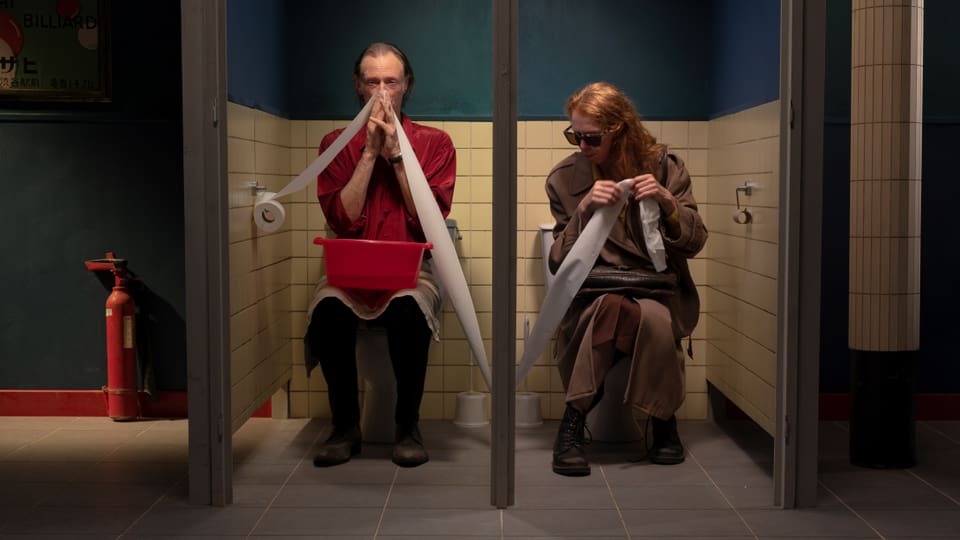 Zwei Menschen sitzen auf einer öffentlichen Toilette.