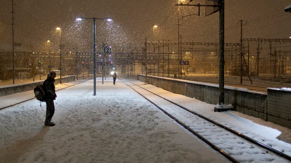 Pendler steht auf verschneitem Perron am Bahnhof