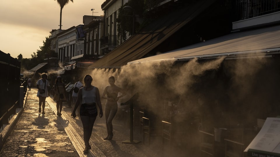Menschen im Athener Stadtteil Monastiraki gehen an einer Nebelmaschine vorbei, um sich abzukühlen.