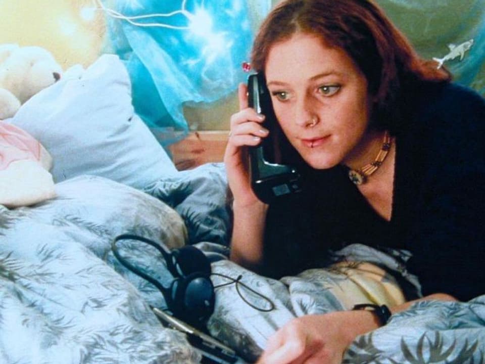 Eine junge Frau liegt auf einem Bett und telefoniert.