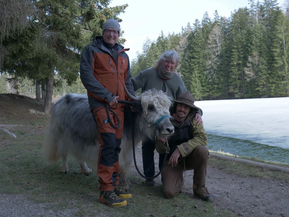 Zwei Männer, ein Yak und ein Hund an einem Bergsee.