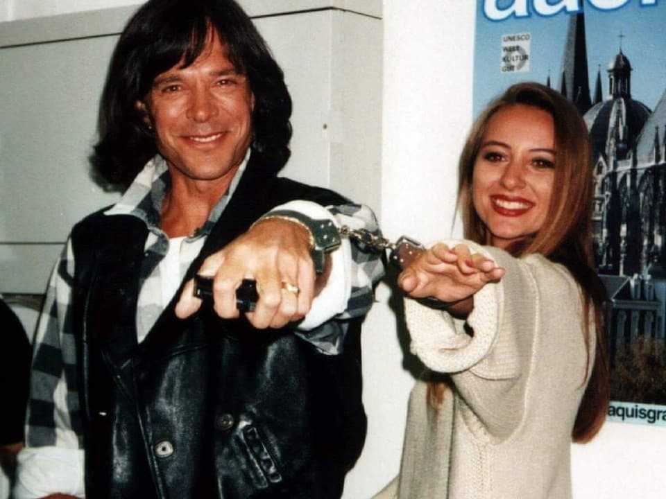 Jürgen Drews und seine zweite Frau Ramona. Die beiden stehen nebeneinander und halten ihre Hände in die Kamera, welche durch Handschellen zusammengehalten werden.