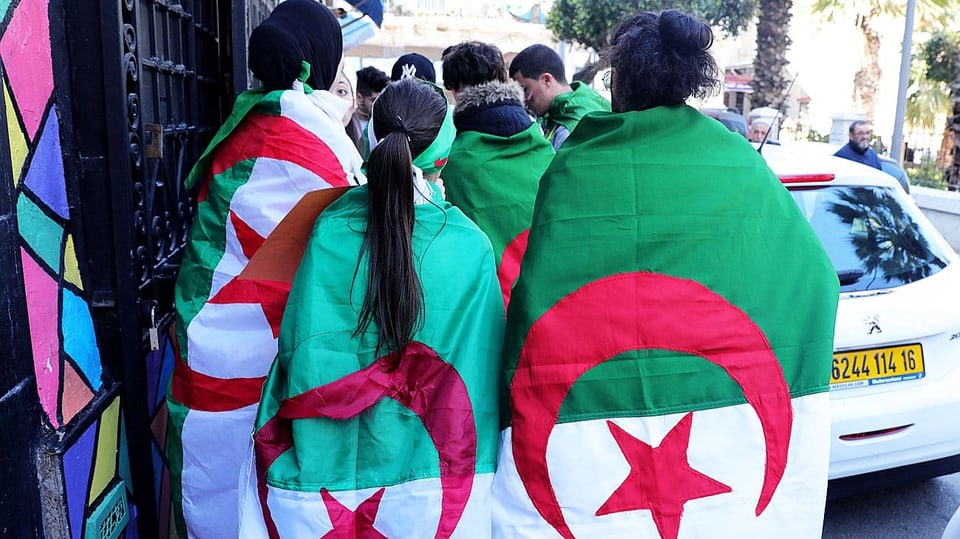Junge Leute laufen auf der Strasse, sie tragen die Algerische Flagge auf dem Rücken.