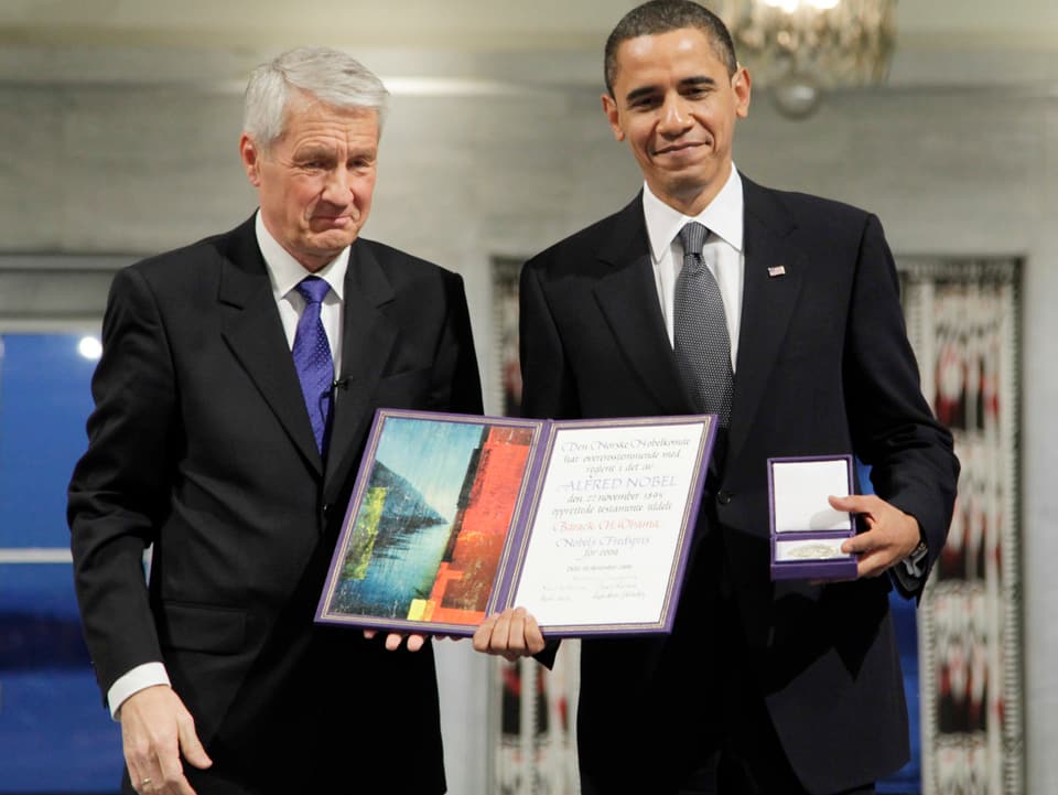 Obama zeigt die Urkunde und die Medaille zu seinem 