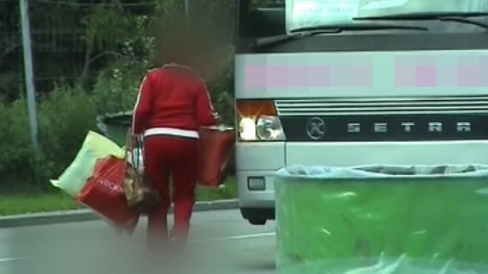 Frau in rotem Trainingsanzug und mit mehreren grossen Taschen steigt in einen Reisebus.