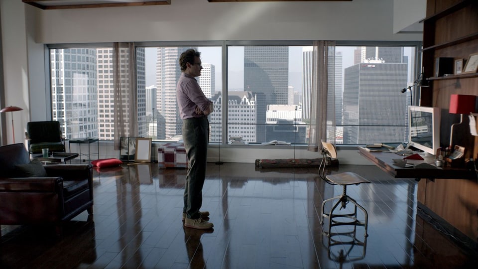 Mann wartend vor einem Computer in New Yorker Wohnung vor Fenster mit Skyline