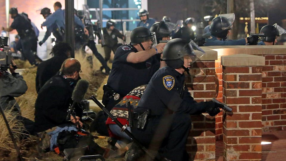 Polizisten in Kampfmontur und gezogenen Waffen gehen hinter einer Mauer in Deckung