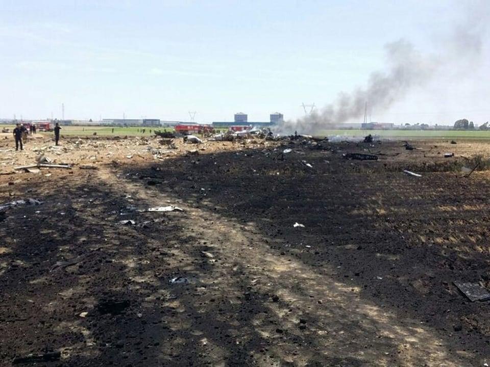 Trümmerteile eines Flugzeugs auf einem verkohlten Feld. 
