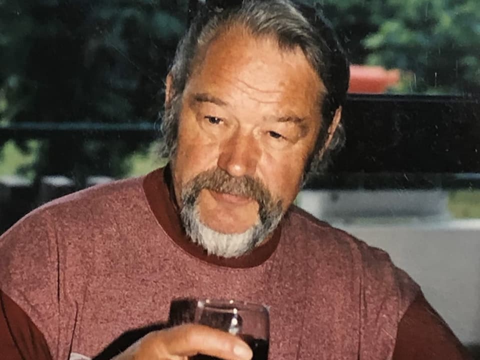 Ein Mann mit Bart hält ein Glas Wein in der Hand.