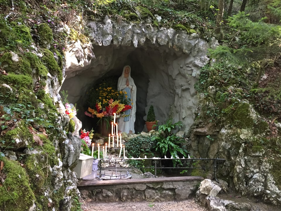 Ausbuchtung in einem Felsen, darin zwei Statuen, davor ein Ständer mit Kerzen