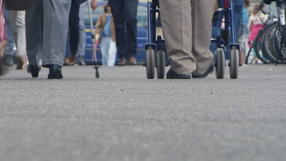 Menschen mit Gehstöcken, Rollatoren und Rollstühlen.