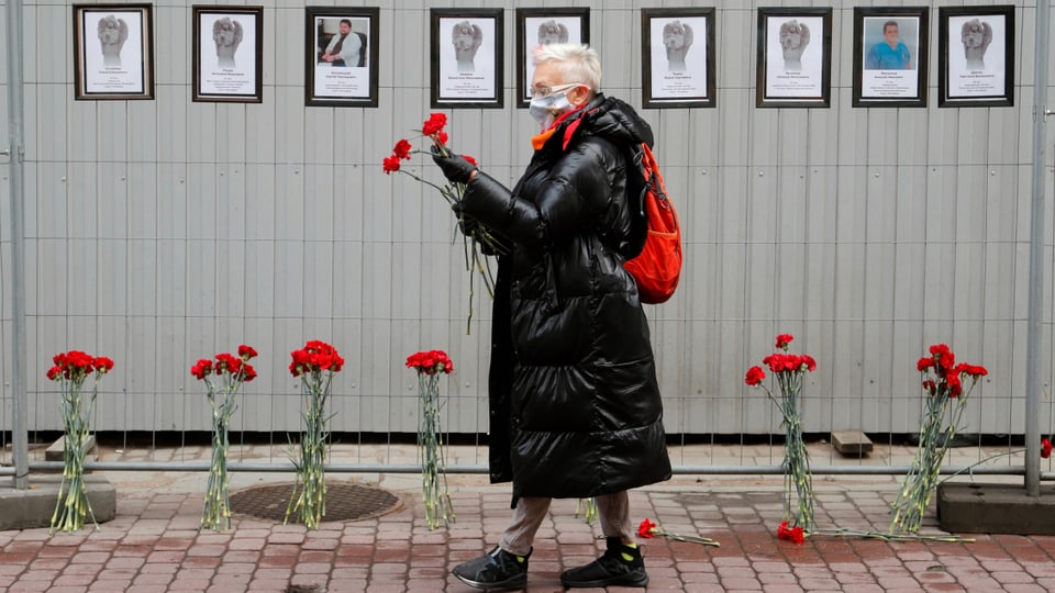 Frau mit Blumen vor einer Wand mit Fotos von Verstorbenen.
