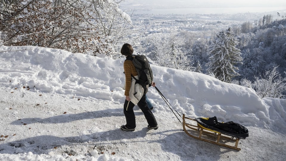 Eine Frau zieht einen Davoserschlitten einen Winterweg hoch.