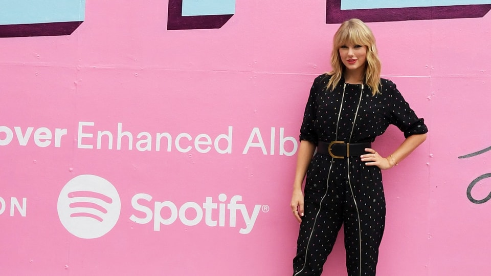 Taylor Swift lächelnd vor dem Spotify-Schriftzug.