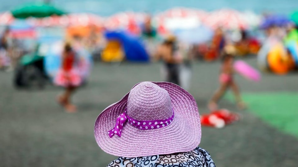 Frau mit violettem Hut steht am Strand