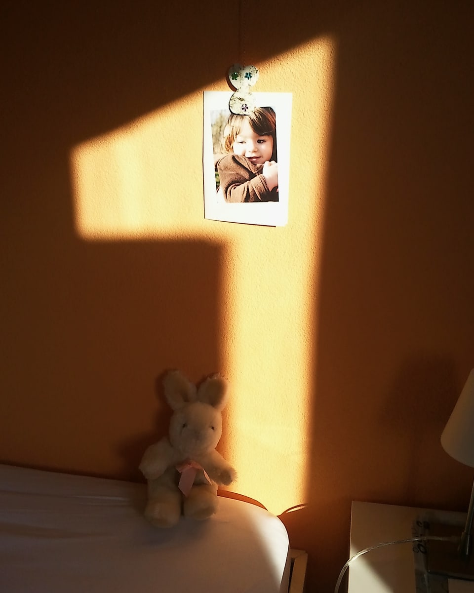 Die Sonne wirft einen Schatten ins Kinderzimmer. Zu sehen ist eine eins auf dem Bild eines Kindes.