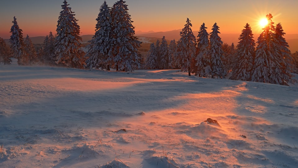 Sonnenuntergang am Creux du Van. Die Bise fegt den Schnee über die Weiden.