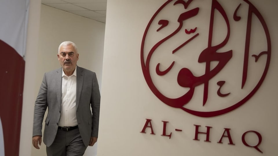 Ein Mann läuft neben einem «Al-Haq»-Logo an einer Wand vorbei