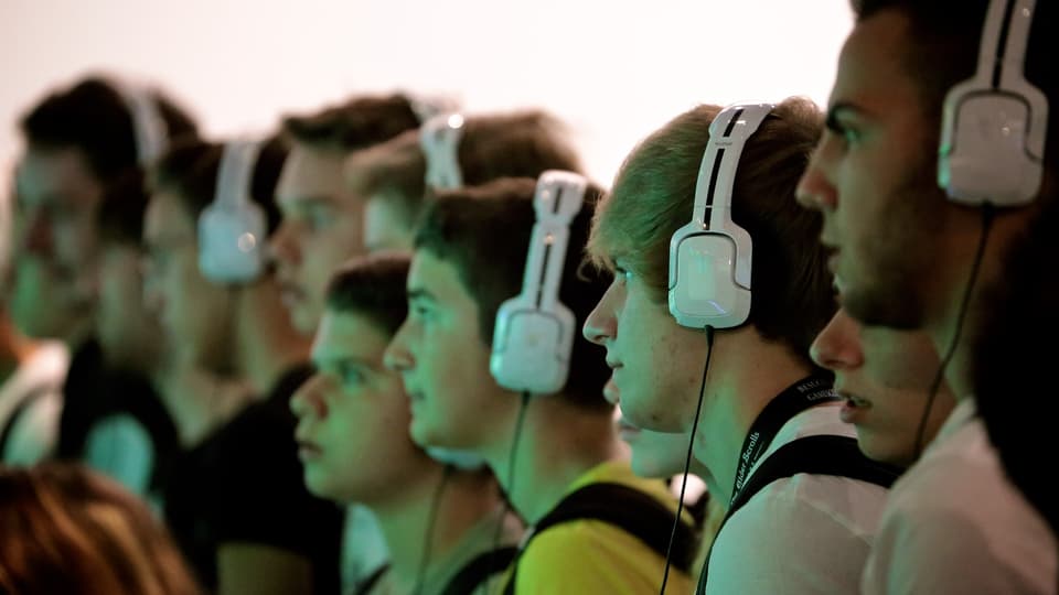Eine Reihe Jungs mit weissen Kopfhörern schaut konzentriert auf ein Fussballspiel.