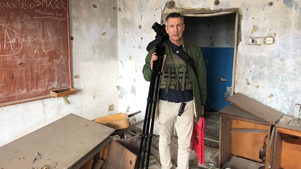 A man with a camera and a tripod in his hand, stands in the filming room and looks at the camera.