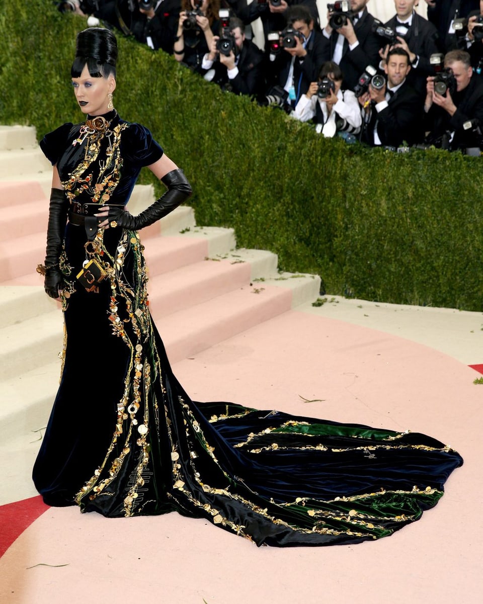 Katy Perry in einem schwarz Goldenen Kleid. Mit Turmfrisur und ungewöhnlichem Make up.
