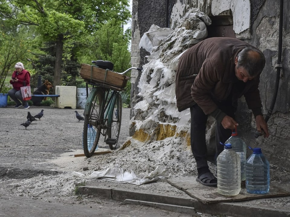 Ein Mann füllt eine Wasserflasche auf, daneben eine kaputte Gebäudefassade.
